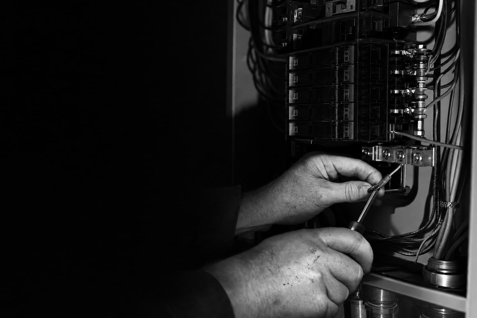 A master electrician’s hands terminate a wire in an open industrial electrical panel.